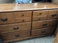 Full front view of a medium-sized wooden dresser with multiple drawers, slightly glossy top with minor scratches