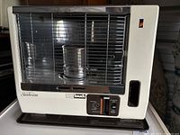 Front view of kerosene heater showing Sunbeam OneTouch branding, control panel with sliding and toggle switches, metal grill and white casing.