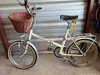 Side view of vintage white ladies bicycle with pink woven basket on front and yellow lock on rear part of frame.