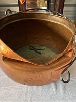 Photo showing the interior of the large copper pot with the detached twisted metal handle lying inside on the bottom, displaying dents and wear.