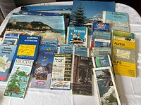 Wide view of the various maps and prints spread out on a table, showing titles and designs of multiple map covers and brochures.
