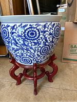 Front view of blue and white ceramic planter on red wooden stand showing floral design and stand wear.