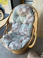 Front view of rattan chair with floral cushion, showing rounded frame and tufted cushion in need of cleaning.