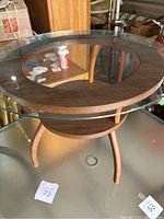 Full view of the round side table showing the oversized glass top with wooden frame and lower shelf.