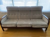 Front view of three-seat beige fabric sofa with tufted back and walnut wood frame