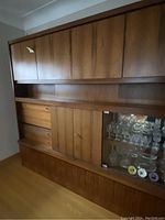 Side angle view of the wall unit focusing on the upper cabinets, drawers, and glass display with glassware inside.