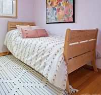 Twin bed set up with light wood frame and bedding in a small room.