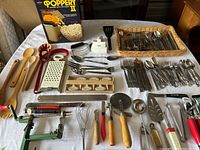 Full overview of cutlery and utensils including wooden cooking spoons, graters, can opener, popcorn popper, knives, forks, spoons, and other kitchen tools.