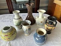 Seven assorted vases displayed on white tablecloth, showing variety in shape, color, and style