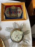 Molson Canadian framed bar sign and Ingraham sunburst metal clock on white cloth background