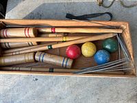 Wooden croquet mallets, colored balls, metal wickets, and wooden stakes in a box.