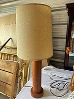 Full view of the vintage table lamp showing the beige fabric shade and cylindrical wooden base on a round platform.