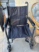 Front view of black driven wheelchair with fabric seat and backrest, showing armrests and front wheels.