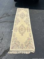 Full view of the wool runner rug laid out on asphalt, showing the overall design and fringed edges.