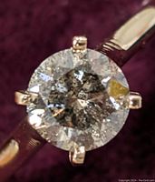 Top view of ring showing round brilliant diamond in 6-prong yellow gold setting on purple background.