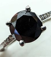 Close-up front view of the round black diamond set in 10K white gold prong setting with part of the textured band visible