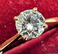 Close-up of round brilliant cut lab-grown diamond set in four prongs on 10K yellow gold band. Diamond facets reflecting light.