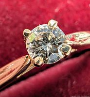 Close-up front view of the ring showing diamond and band engraving on red background.