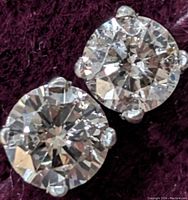 Pair of round diamond studs on burgundy fabric background, angled view showing size and setting