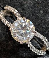 Close-up of the 14K white gold moissanite ring showing the center round cut stone and pavé-set accent stones on split-shank band.