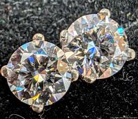 Front view close-up of both round brilliant moissanite stones in four-prong white gold settings on black background