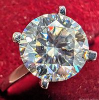 Top view of ring showing round brilliant cut moissanite in four prong 14K white gold setting on red background