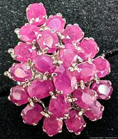 Close-up photo of silver ring set with multiple oval natural ruby stones arranged in a cluster design on a black background.
