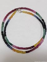Full view of multicolor sapphire and emerald faceted bead necklace coiled with visible clasp.