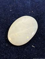 Close-up image of oval genuine Australian opal with light flashes, showing polished domed surface on dark fabric background.