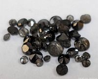 Loose black diamond stones shown scattered on white background, varying sizes and round faceted cuts visible.