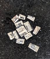 Close-up of multiple small rectangular shape genuine diamonds on a black cloth surface.