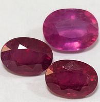 Close-up of three oval faceted ruby gemstones with varying red hues.
