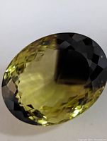 Oval cut faceted yellow-green gemstone showing color, facets, and shape clearly.