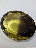 Top view of large faceted oval gemstone showing yellow to brown color gradient and checkerboard cut pattern.