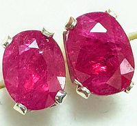 Close-up view of the front sides of the ruby earrings showing the faceted deep red oval rubies set in four-prong silver mountings.