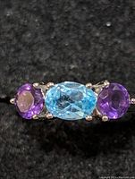 Close-up top view of sterling silver ring showing blue topaz center stone and two amethyst stones on either side.
