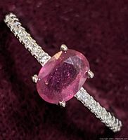 Close-up image of sterling silver ring with oval pink ruby center stone and cubic zirconia stones on the band