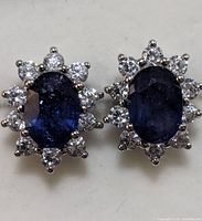 Close-up front view of pair of sapphire and CZ stud earrings on white surface.