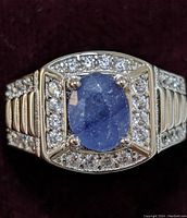 Close-up front view of the sterling silver ring featuring a cushion-shaped blue sapphire center stone surrounded by clear cubic zirconia stones on a ridged band.