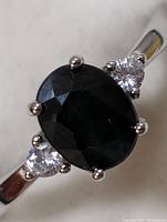 Close-up front view of the ring showing the oval sapphire center and two round cubic zirconia stones with sterling silver band.