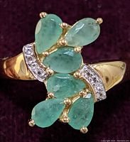 Close up front angled view of the gold-tone sterling silver ring showing pear-shaped emerald stones with white topaz accents.