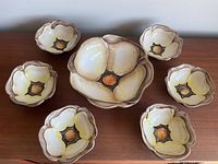 Photo showing one large central flower-shaped ceramic bowl surrounded by six smaller matching bowls, highlighting the floral design and color scheme.