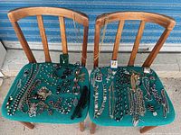Two green fabric-covered chairs with assorted costume jewelry including necklaces, bracelets, rings, and earrings arranged on the seats.