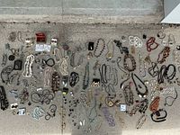 Wide view displaying an assortment of costume jewelry items laid out on the ground: multiple necklaces, bracelets, earrings, and rings in various styles and colors.