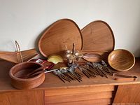 Overall view of teak serveware, bowls, basket, condiment caddy, flatware and plates on wooden surface