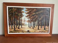 Framed oil painting of a forest landscape with autumn trees and light clearing, in a brown wooden frame with white inner border.