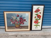 Two framed floral art pieces resting against blue metal door. One horizontal, one vertical.