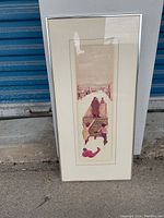 Full front view of framed artwork leaning against panel and metal door