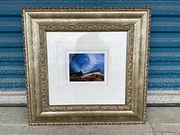 Front view of framed artwork showing the painting centered within a wide mat and ornate silver-gold tone frame.