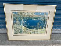 Full view of framed art print showing lake scene with trees and boats; some glare on glass.